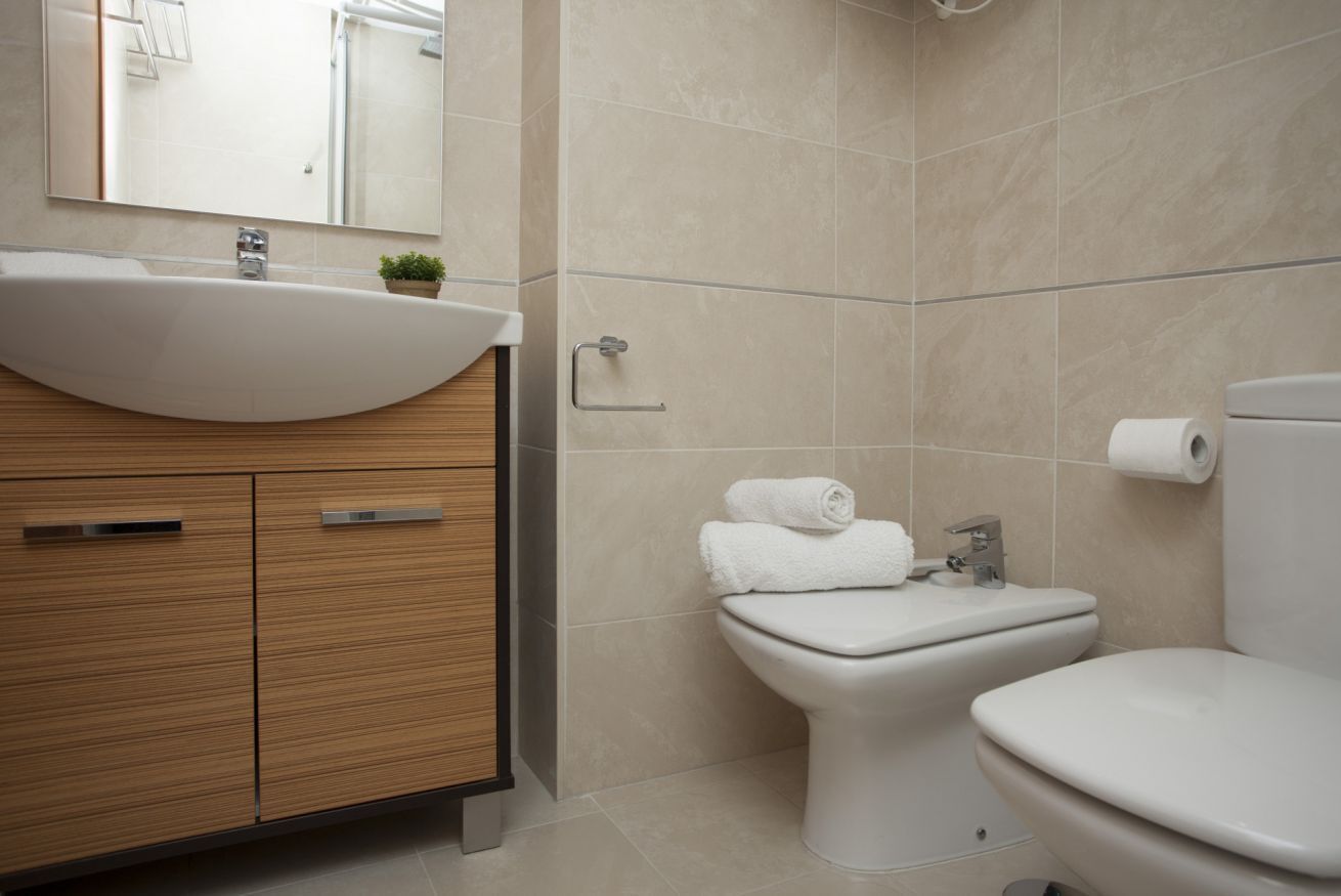 A modern bathroom with a wooden vanity, a sink, a toilet, and a mirror.