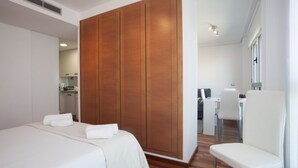Een hotelkamer met een bed, een houten garderobe, een zithoek met een tafel en stoelen, en een witte stoel.