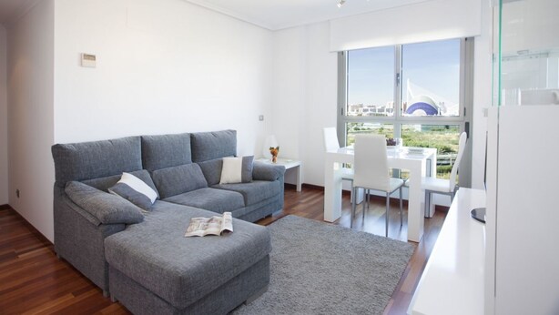 Een moderne woonkamer met een grijze bank, een kleine tafel en een eethoek met stoelen.