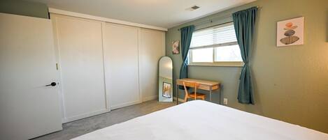 A bedroom with a bed, a desk, a chair, a mirror, and a window with curtains.
