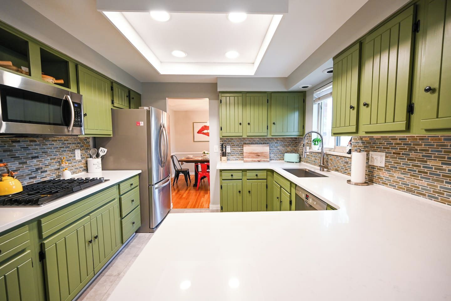 A modern kitchen with green cabinets, a stainless steel refrigerator, and a skylight.