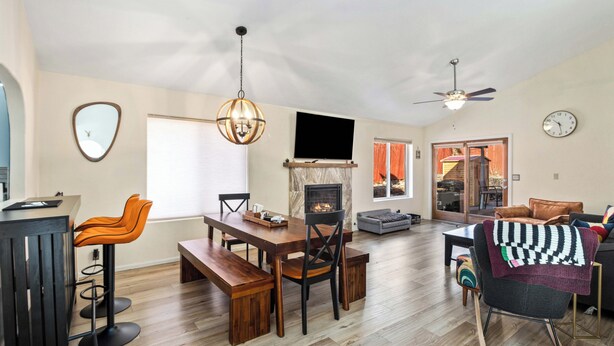 Amplia sala de estar con una mesa de comedor de madera, dos taburetes de bar, chimenea, sofá y ventilador de techo.