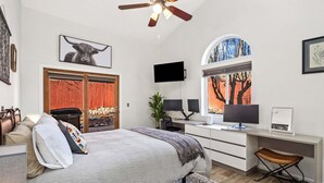 Un dormitorio con cama, escritorio, silla, televisor y ventana con vista a un árbol.