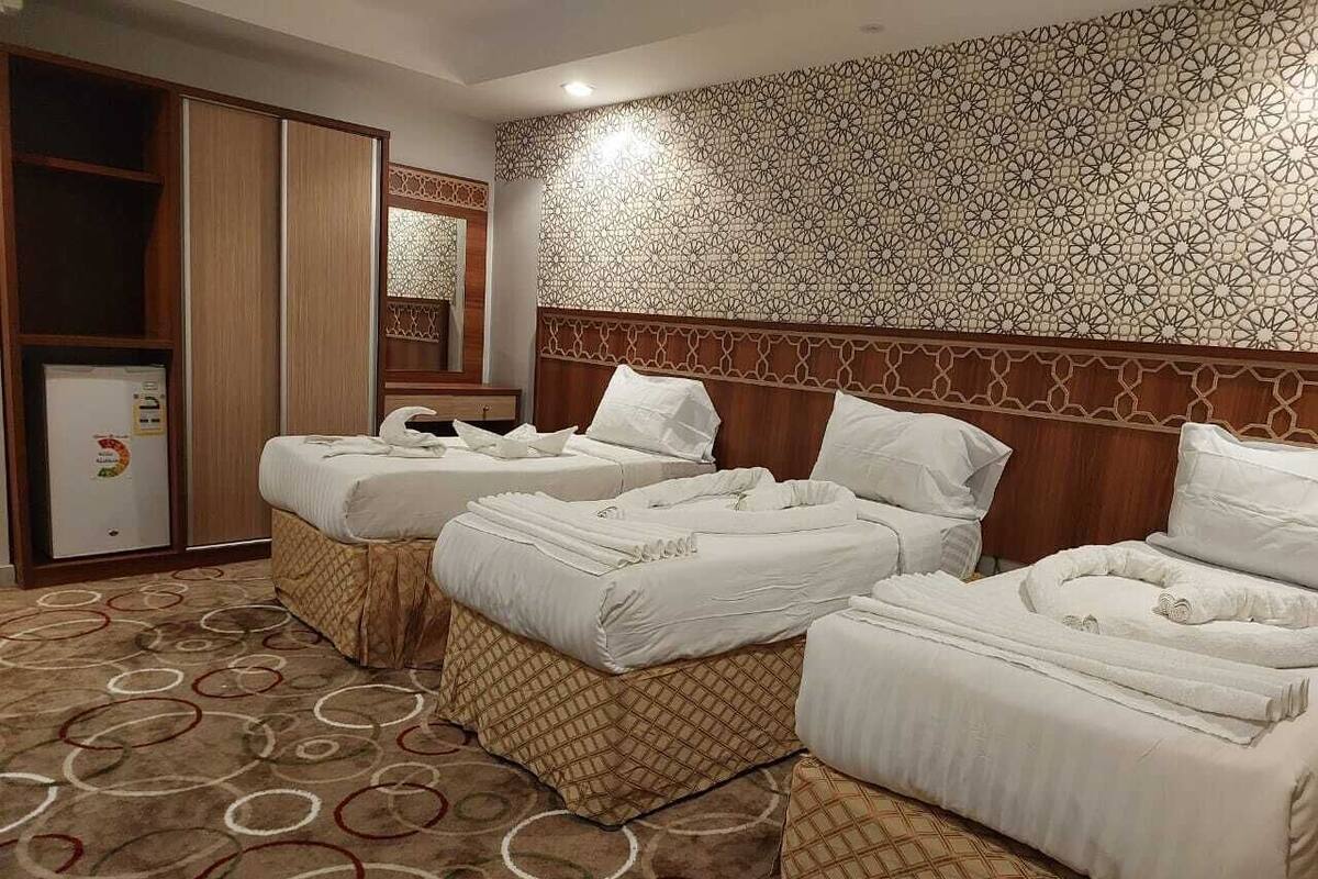 Habitación de hotel con tres camas, un armario, un minibar y una alfombra estampada.