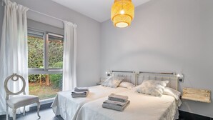 Ein Schlafzimmer mit zwei Betten, einem Sessel, einem Fenster mit Vorhängen und einer Pendelleuchte.