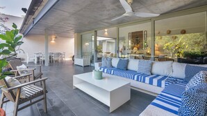 Eine Terrassengruppe im Freien mit einer weißen Couch, blauen und weißen Kissen, einem weißen Couchtisch und Holzsesseln.