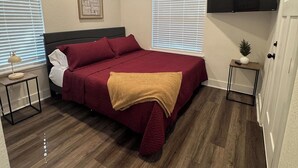 Ein Schlafzimmer mit Bett, Deckenventilator, montiertem Fernseher und einem kleinen Tisch mit Lampe.