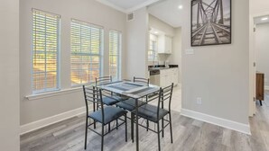 Uma área de jantar com uma mesa e cadeiras, uma cozinha ao fundo e um quadro na parede.