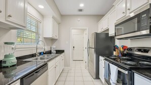 Cozinha moderna com armários brancos, bancada preta, geladeira de aço inoxidável, fogão e liquidificador.