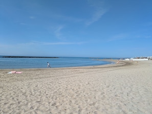 A beach with a clear sky, a sandy shore, and a rocky breakwater in the distance.