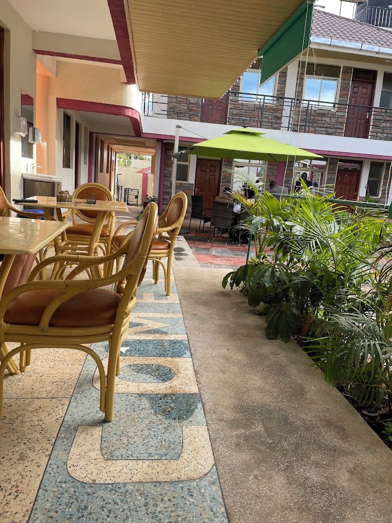 A courtyard with outdoor seating, including wicker chairs and tables, surrounded by potted plants and a tiled floor.