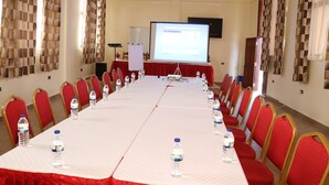 A conference room with a long table, red chairs, water bottles, and a projector screen. - The Haven Luxury Guest House moyale (Moyale)
