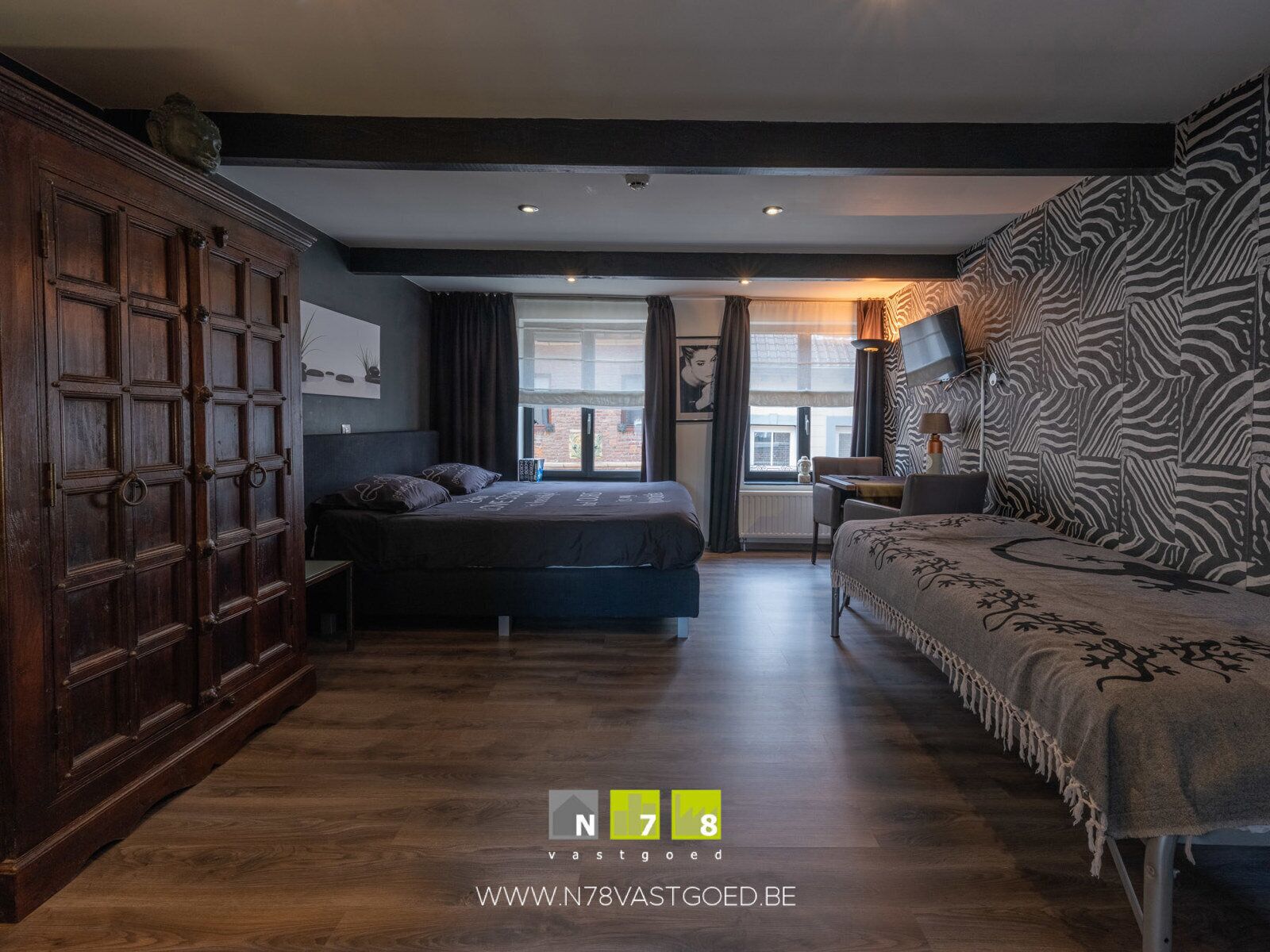 A modern hotel room with a large wardrobe, a bed, a sofa, and a view of the city.