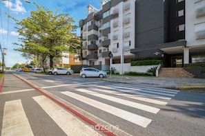 Un immeuble résidentiel à plusieurs étages, doté de balcons, d’un passage piéton et de voitures garées.