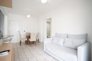 Ein modernes, minimalistisches Wohnzimmer mit einem weißen Sofa, einem Esstisch mit Stühlen und einem Deckenventilator.