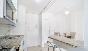 A modern kitchen with granite countertops, a built-in stove, and a sink. There is a dining area with a table and chairs, and a white door leading to another room. - Apt 700 m From Praia de Jurere Aav0306 (Florianópolis)