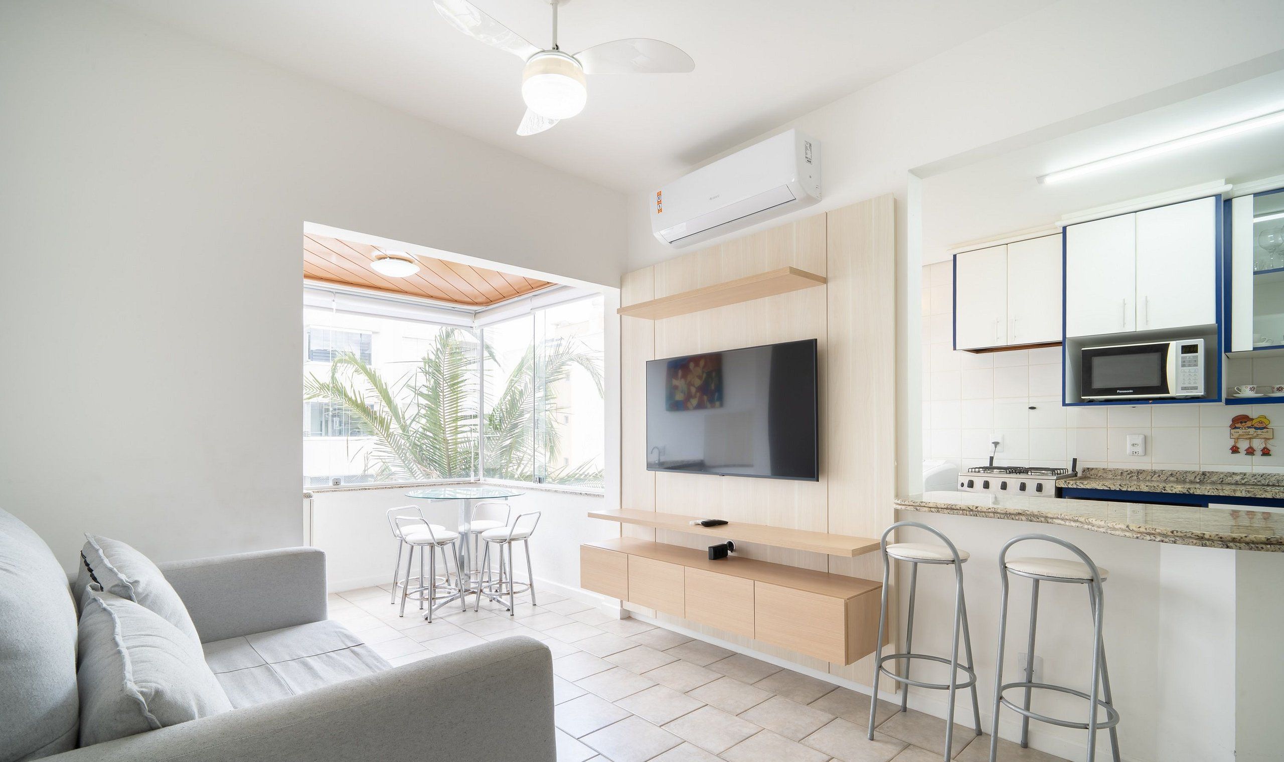 Una sala de estar moderna con televisor de pantalla plana, un sofá, un comedor con sillas y una cocina con microondas y armarios.