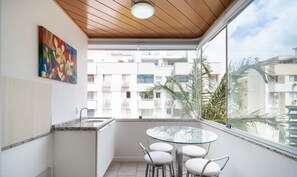 A balcony with a glass table and chairs, a sink, and a painting on the wall. - Apt 700 m From Praia de Jurere Aav0306 (Florianópolis)