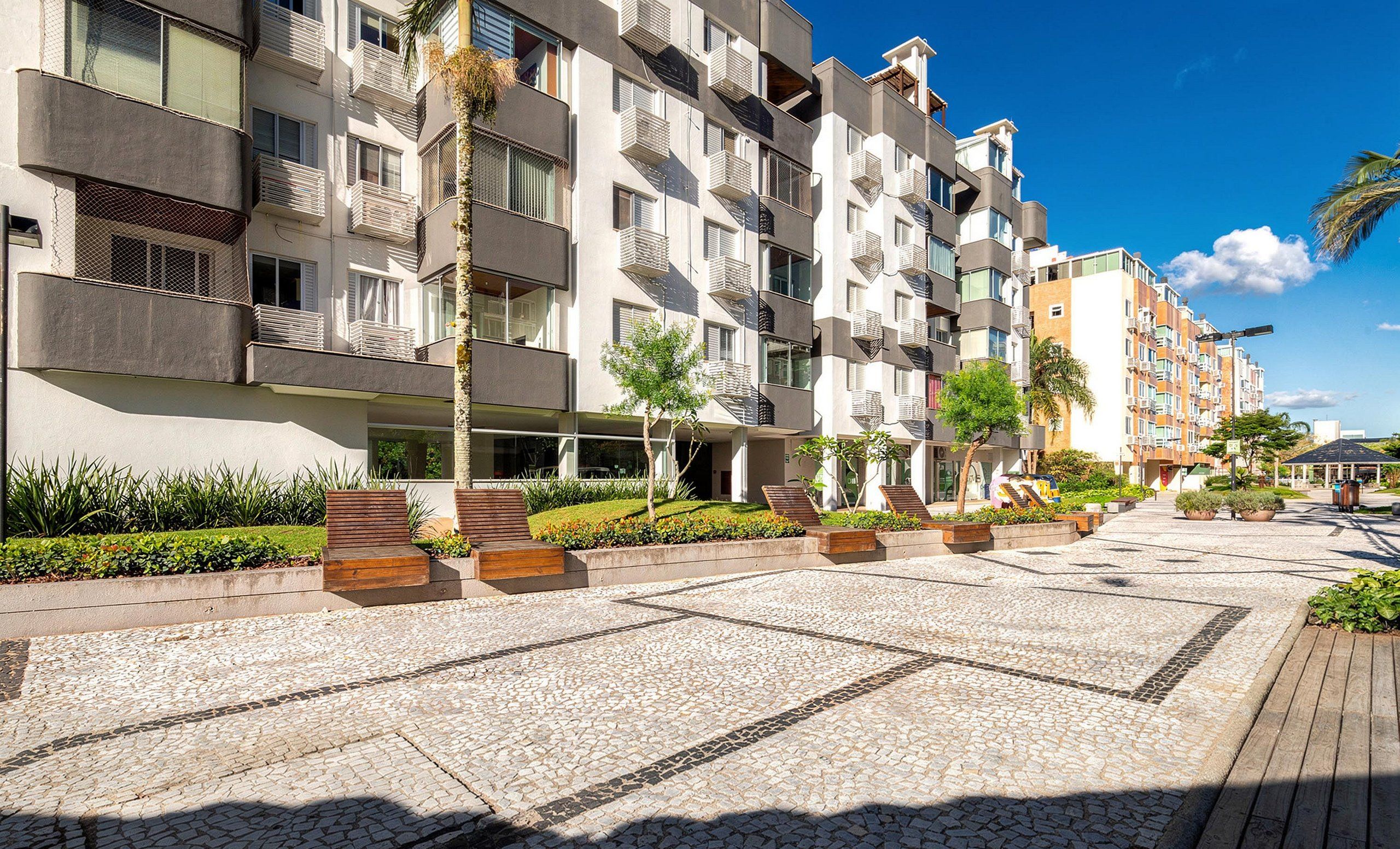 A modern apartment building with balconies, a paved courtyard, and small trees.