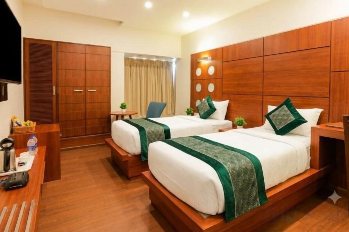 A hotel room with two beds, a desk, a chair, and a wardrobe.