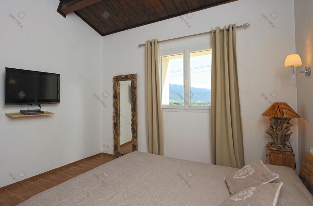 Ein Schlafzimmer mit Bett, Fernseher auf einem Regal, einem Fenster mit Vorhängen und einer Lampe.