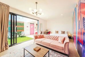 A modern hotel room with a large sliding glass door leading to a patio, a pink sofa, a wooden coffee table, and a bed with a nightstand. - 1 BDRM Suite for Any Budget, Private In-Suite Plunge Pool, Near Eagle Beach (Oranjestad)