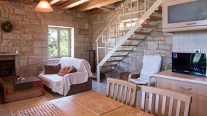 A cozy room with a stone wall, a fireplace, a sofa, a wooden table, a TV, and a staircase. - Pantanassa Villas - Erato with Sea View (Agia Marina)