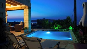 A swimming pool with lounge chairs, a stone wall, and a view of the sea at dusk. - Pantanassa Villas - Erato with Sea View (Agia Marina)