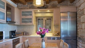 A modern kitchen with wooden cabinets, a stainless steel refrigerator, and a dining area with a wooden table and chairs. - Pantanassa Villas - Erato with Sea View (Agia Marina)