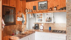 Une cuisine avec des poutres en bois, des meubles blancs, un mur en pierre et une cuisinière à gaz.