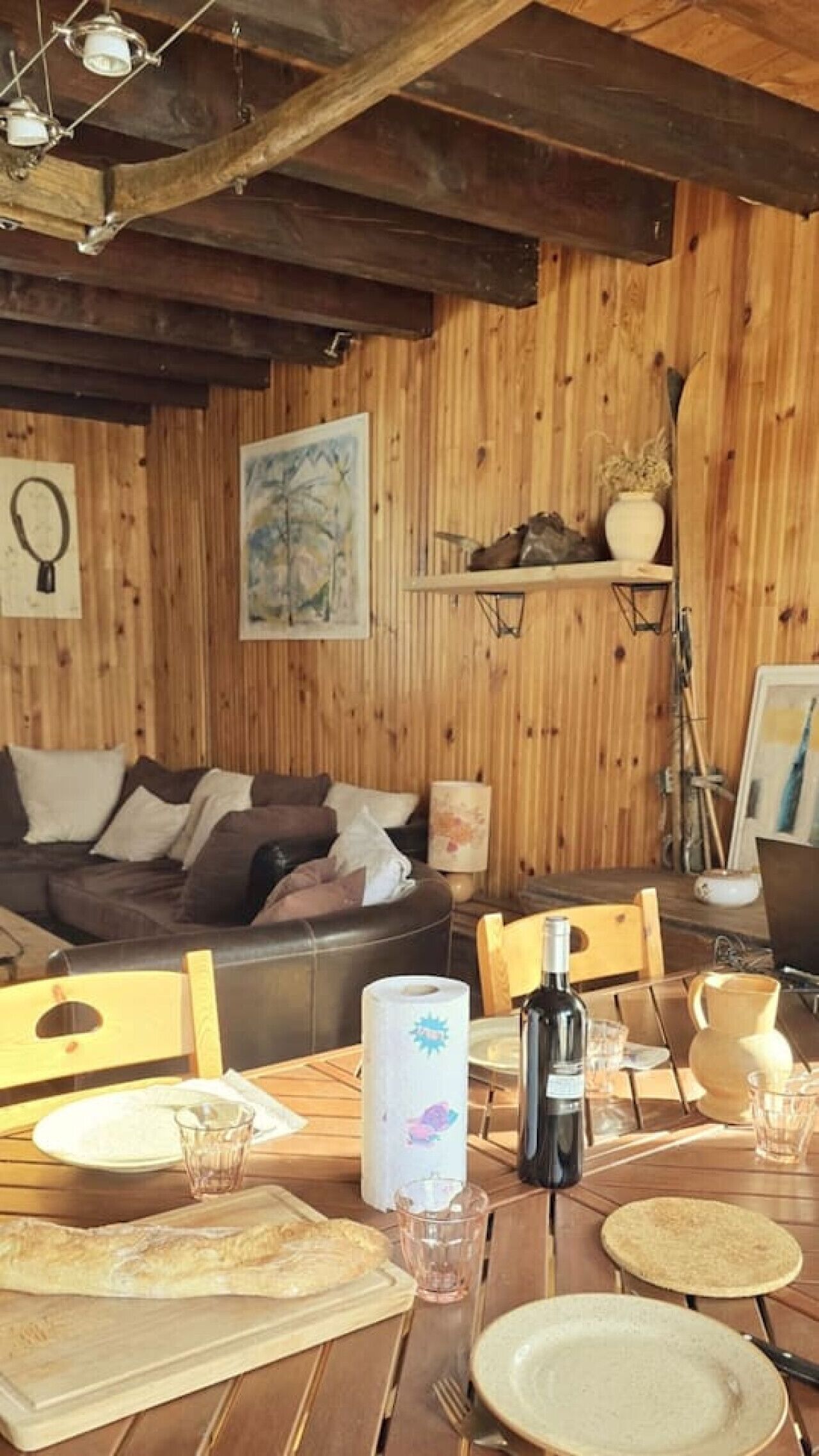 A cozy dining area with wooden walls, a wooden table set for two, and a sofa in the background.