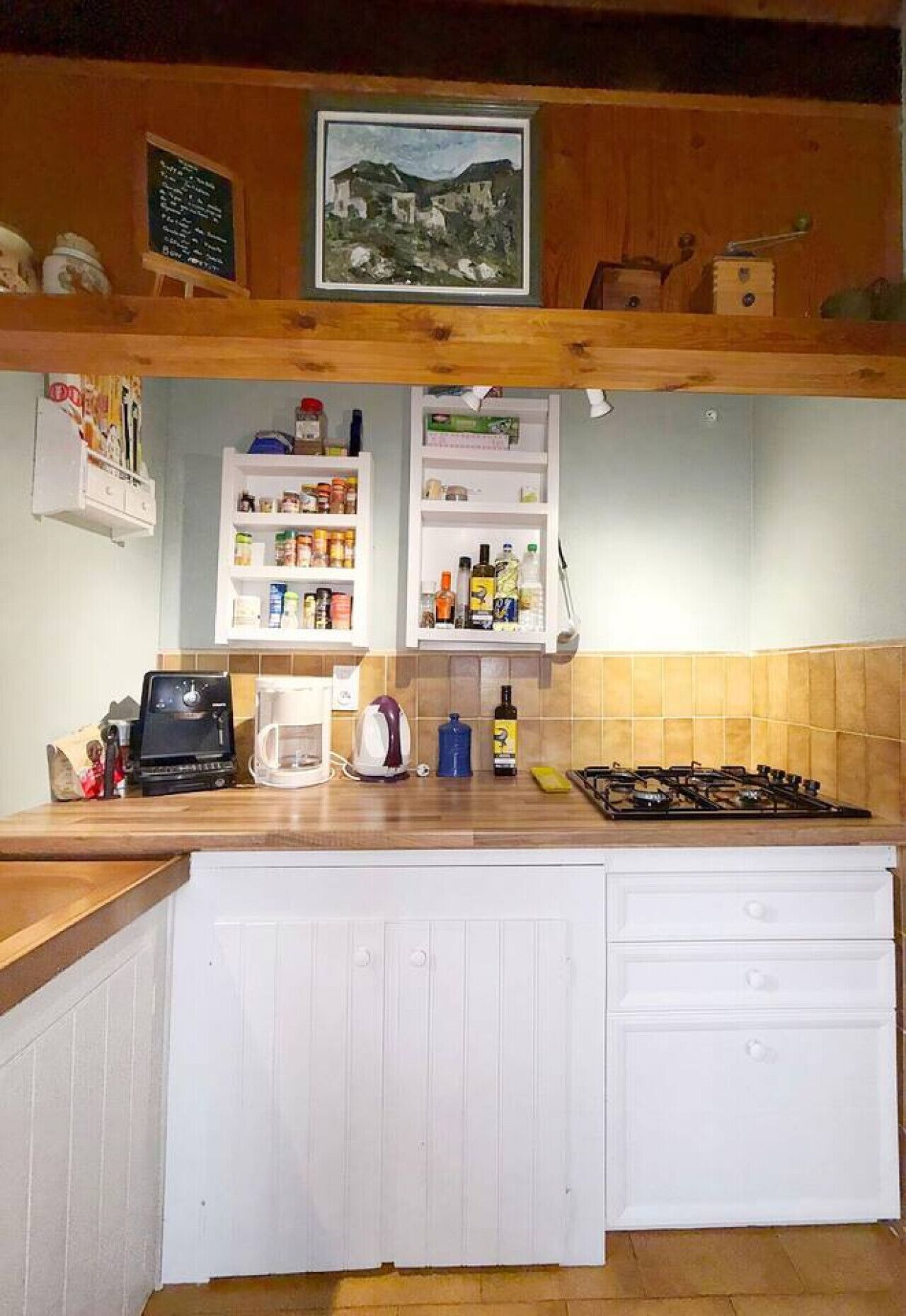 A kitchen with a wooden countertop, a coffee maker, a kettle, and a gas stove. There are shelves above the counter holding various kitchen items.
