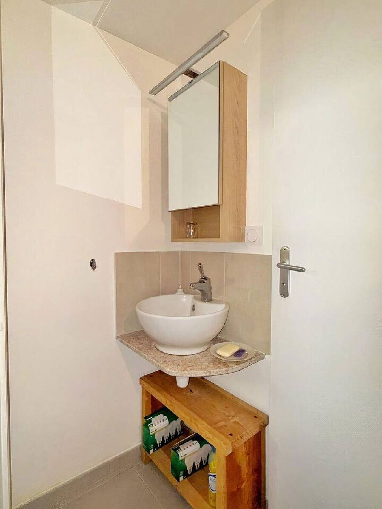 Een badkamer met een wit wastafelmeubel, een spiegel erboven en een houten plank eronder.