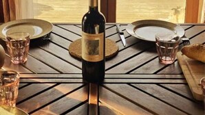 Une table à manger, dressée avec des assiettes, des verres et une bouteille de vin, placée devant une porte vitrée qui offre une vue sur un paysage enneigé.
