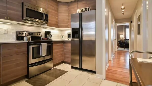 A modern kitchen with stainless steel appliances, wooden cabinets, and a visible 'TAXI' sign on the refrigerator.