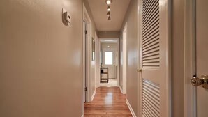 A hallway with wooden flooring, white walls, and a ceiling light fixture.