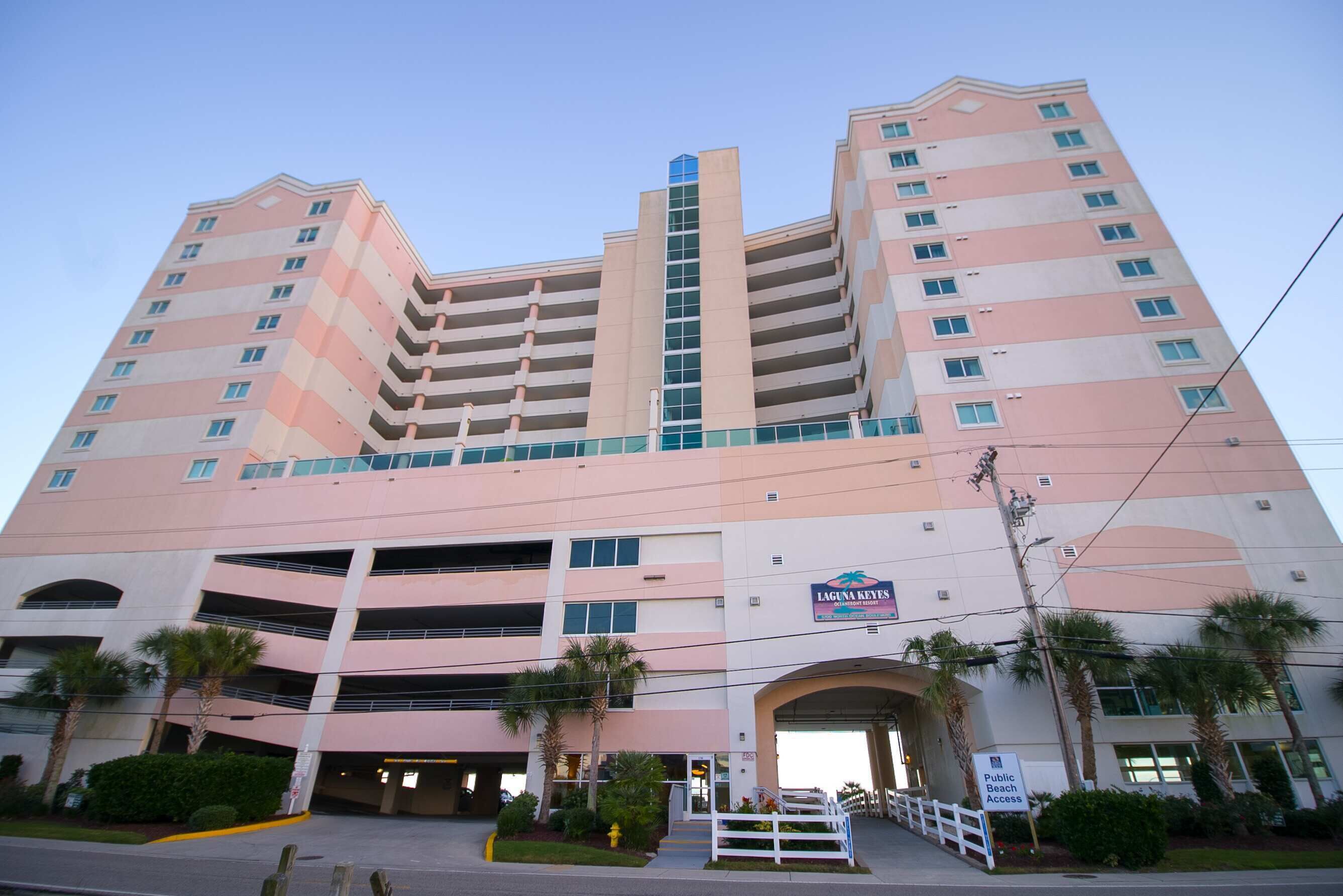 A multi-story hotel with a central vertical feature, a parking garage, and a public beach access sign.