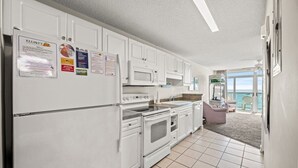 Una cucina con mobili bianchi, un forno a microonde e un frigorifero. Ci sono avvisi sulla porta del frigorifero.