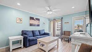 Ein Zimmer mit einem blauen Sofa, einem weißen Tisch, einem Deckenventilator und Blick nach draußen durch ein Fenster.