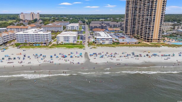 Ein Küstenhotelbereich mit mehreren Gebäuden, einem Strand mit vielen Sonnenschirmen und einem hohen Hotelgebäude.