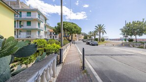 A coastal street with multi-story buildings, a paved sidewalk, and parked cars. - Next to the Beach by Wonderful Italy (Ospedaletti)