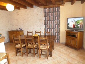 A dining area with a wooden table and chairs, a television on a wooden stand, and a bookshelf in the background. - Gite l'Opale, 3-star, 20 min. from Chambord Castle (Lailly-en-Val)