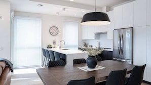 Una cocina moderna con una isla central, electrodomésticos de acero inoxidable y un comedor con una mesa grande y sillas.