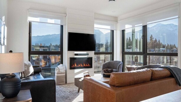 Una sala de estar moderna con chimenea, televisor de pantalla plana y ventanas amplias que ofrecen vistas a la montaña.