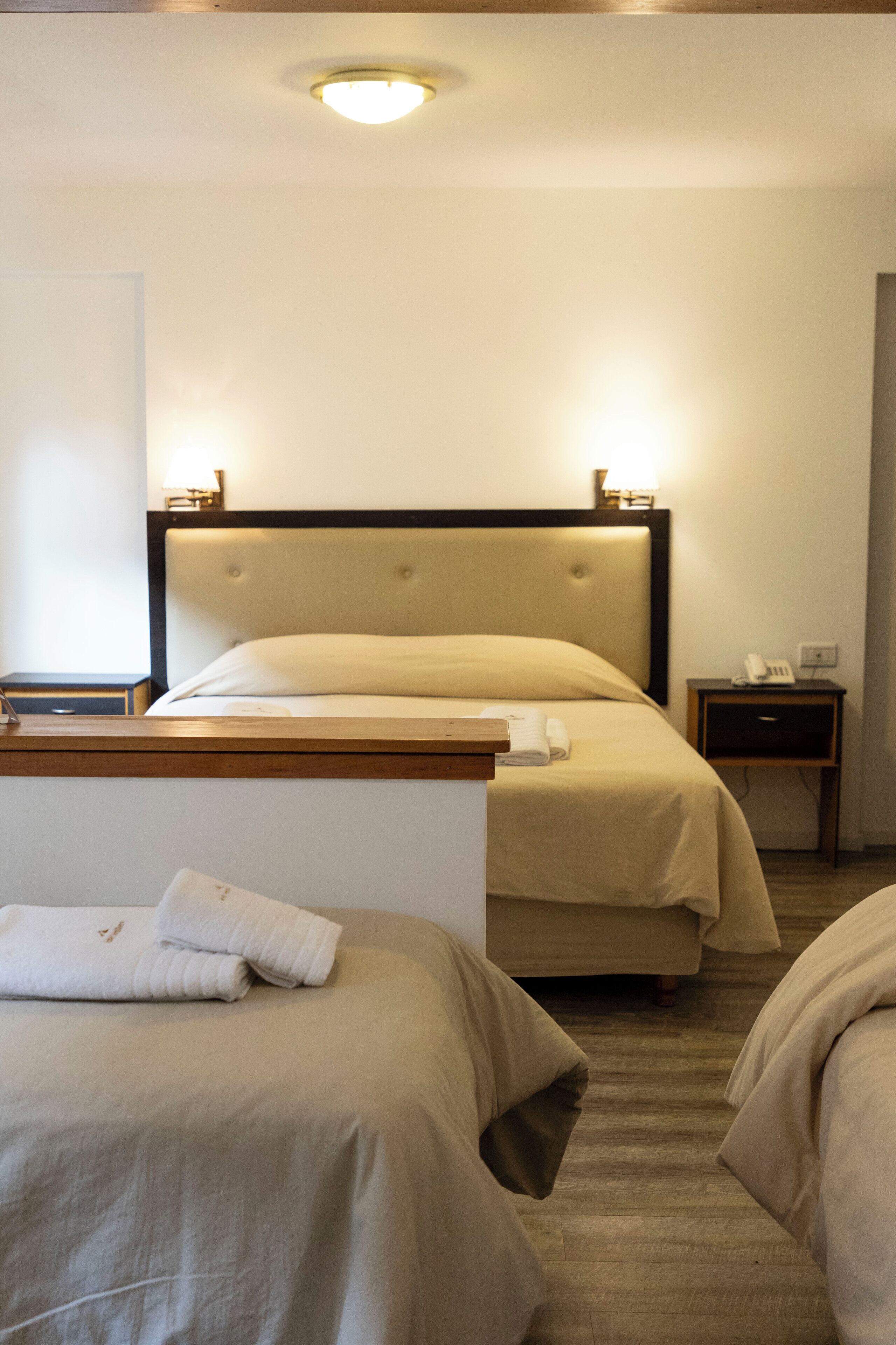 Una habitación de hotel con dos camas, una mesita de noche y una lámpara en el techo.