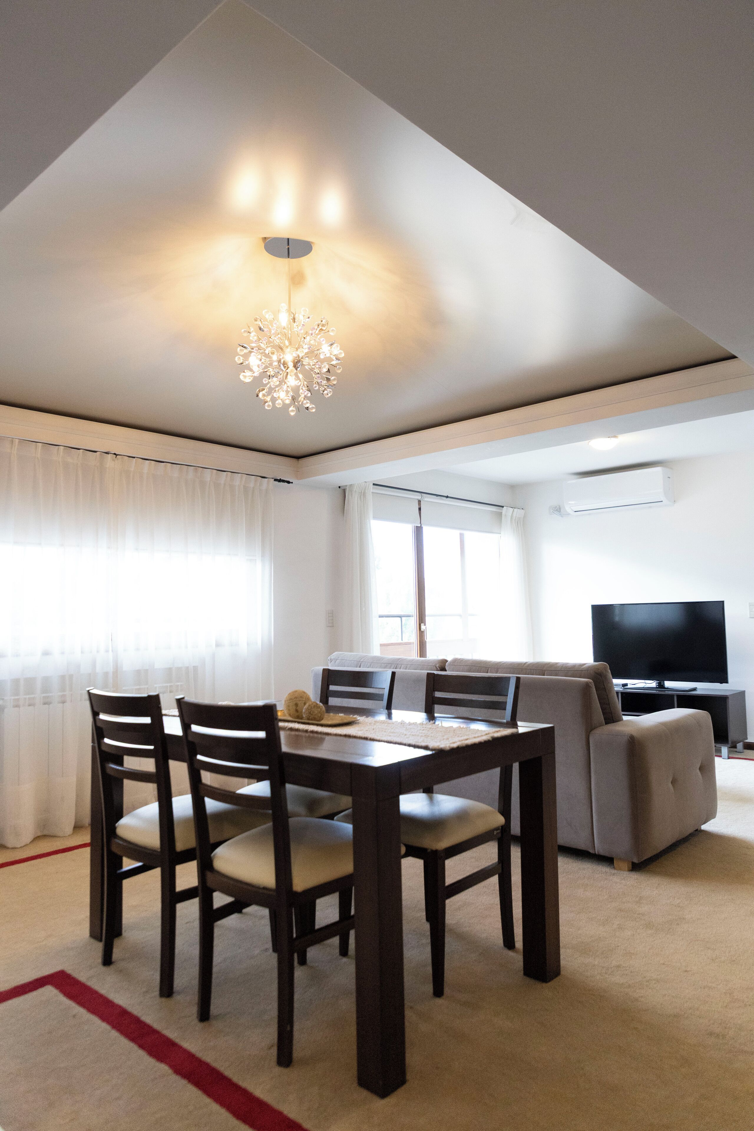 Una sala moderna con comedor, sofá, televisor y candelabro.