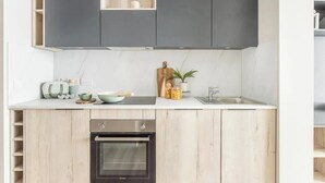 Une cuisine moderne avec des meubles gris, un plan de travail blanc et un four encastré.