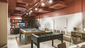 Un espace de détente moderne avec un baby-foot, des sièges confortables et un téléviseur diffusant une chaîne de sport.
