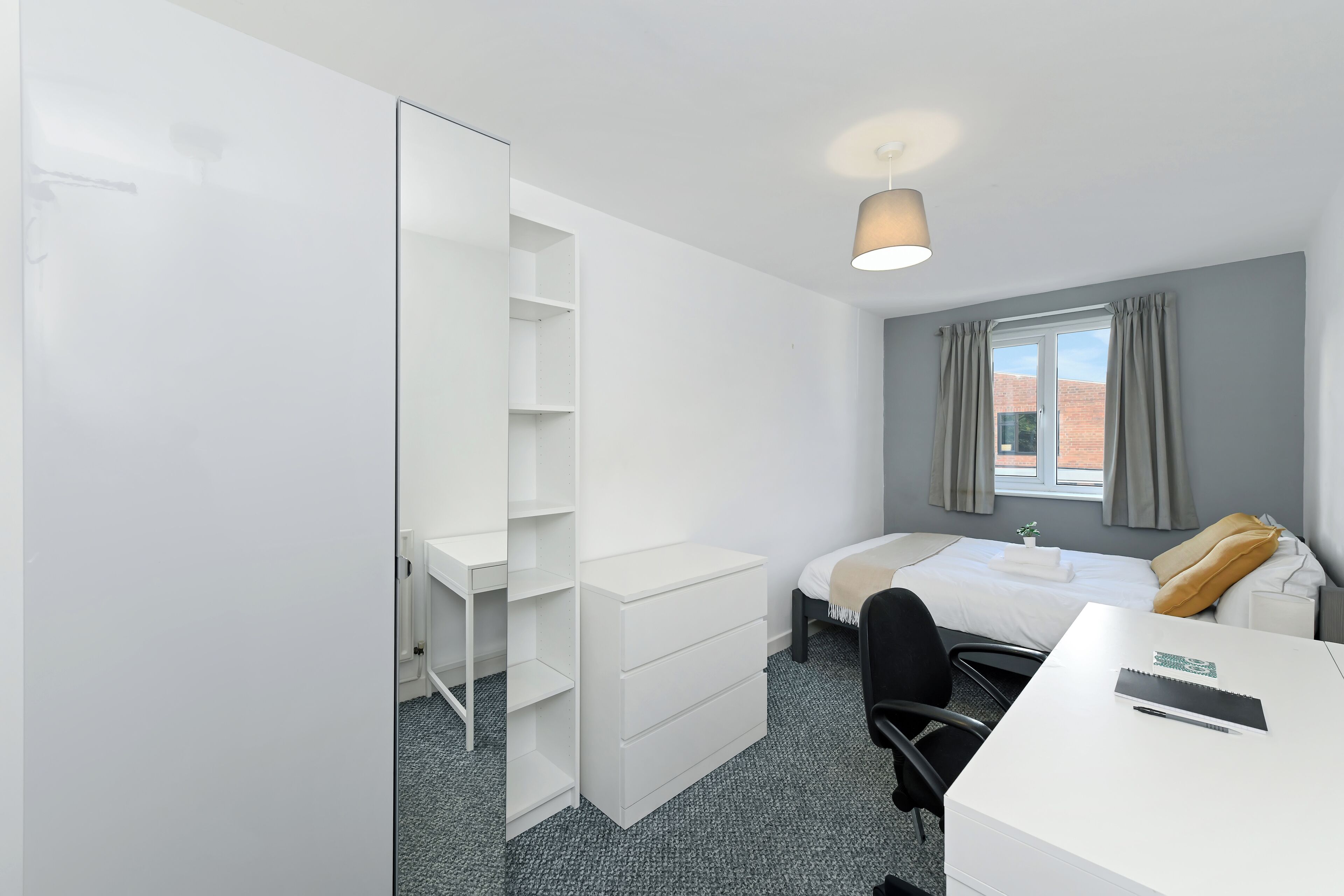 Une chambre d’hôtel avec un lit, un bureau, une armoire et une fenêtre avec des rideaux.