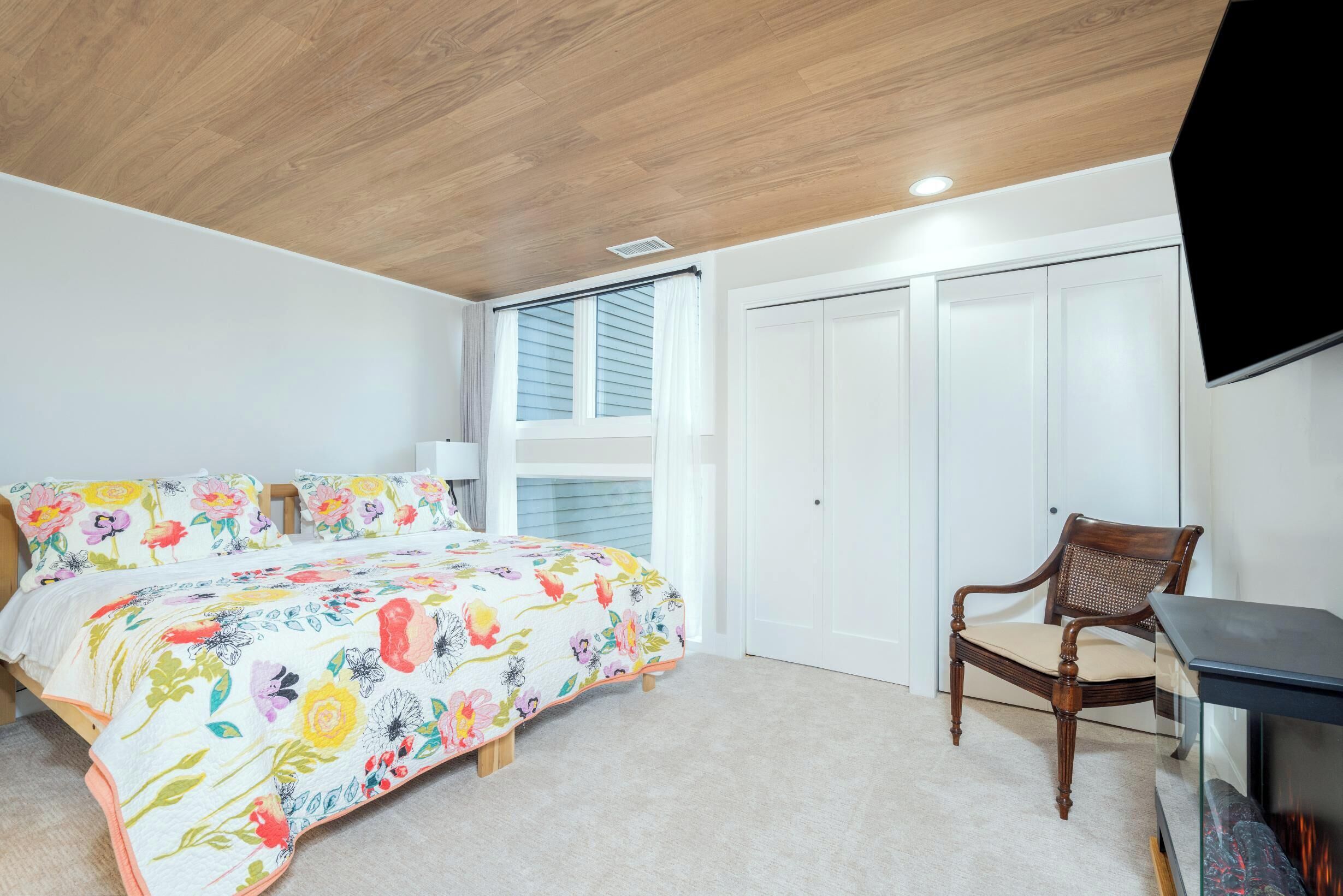 A bedroom with a bed, a chair, a desk, and a TV.